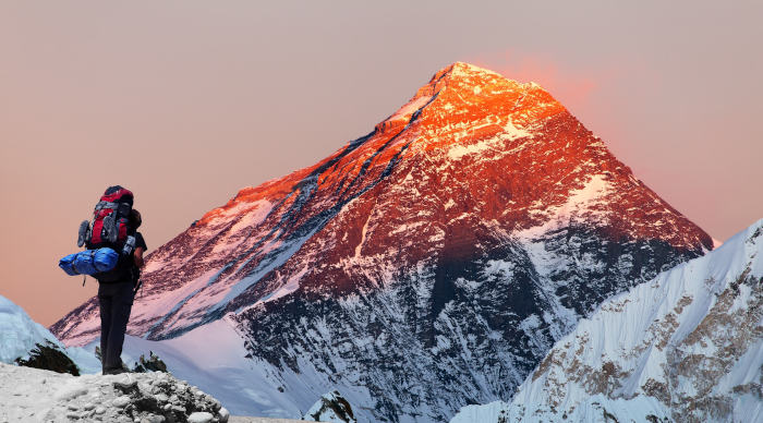 Mann mit schwerem Reisegepäck blicke aus der Ferne auf Mount Everest, der rot von der Sonne angeschienen wird