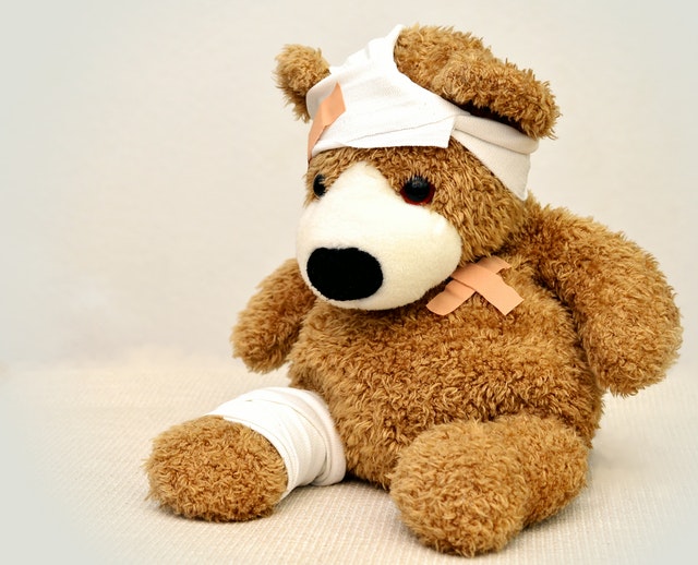 Teddybär, der verletzt ist und am Bein und am Kopf einen Verband angelegt bekommen hat