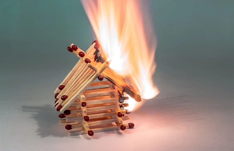 Miniaturhaus aus Streichhölzern, bei dem die rechte Seite bereits in Flammen steht