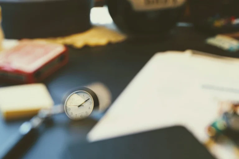 Verschwommene Aufnahme eines Schreibtischplatte, auf dem vage Papier, eine Uhr und Schreibutensilien zu erkennen sind
