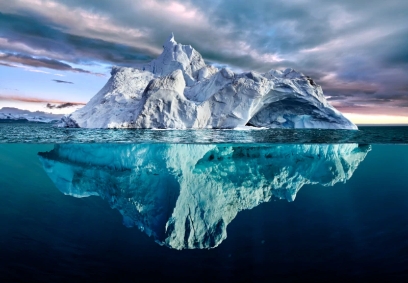 Seitenansicht eines Eisberges, bei dem sowohl der Teil über als auch unter Wasser sichtbar ist.