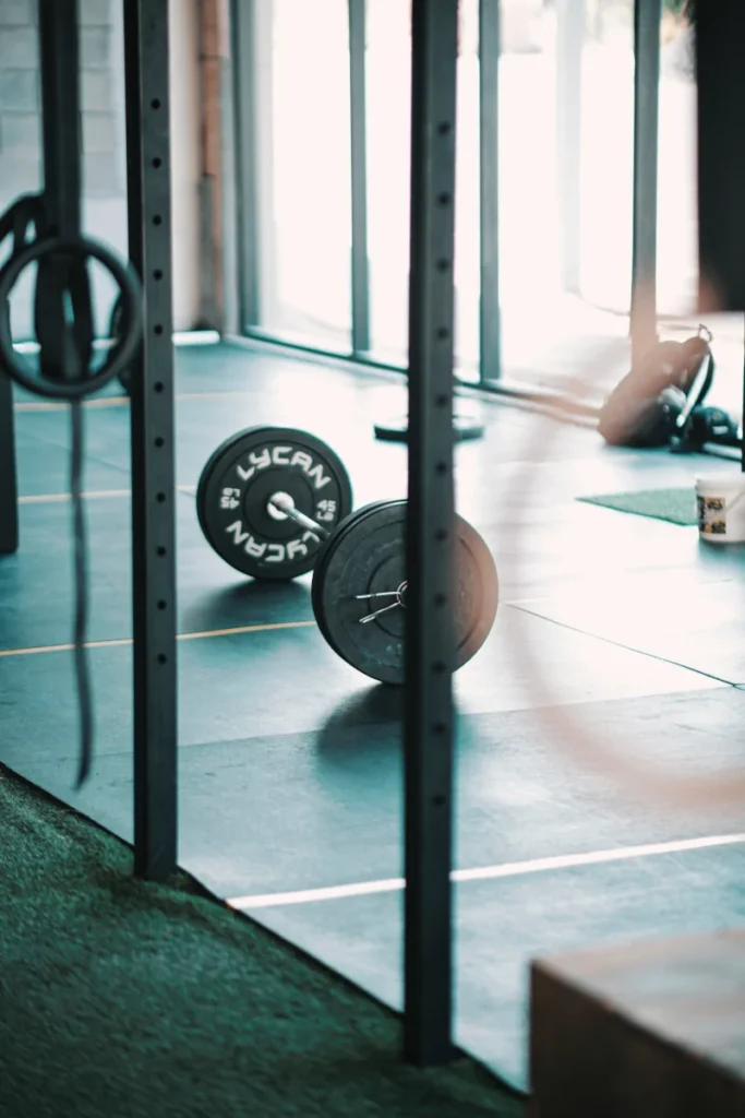 Foto in einem Fitnessstudio, in dem man vorbei an Haltestangen am Boden eine Langhantel mit Gewichtsscheiben sieht.