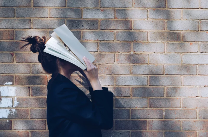 Mensch mit einer High Bun Frisur im Profil hält sich ein Buch vor das Gesicht.