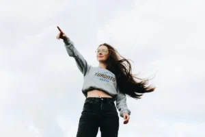 Foto einer Frau, die mit ausgestrecktem rechten Arm und Zeigefinger nach vorne zeigt; Fotografie von unten. Matapher für Stärke, Power und Zufriedenheit - starke Frauen.