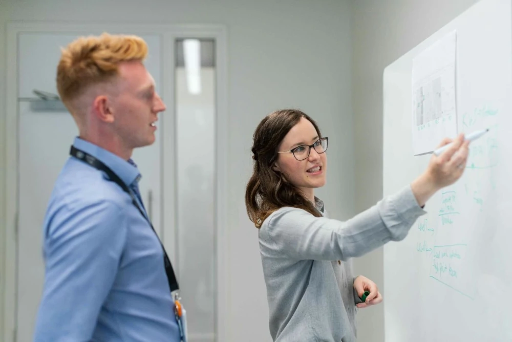 Ein Mann und eine Frau stehen vor einem Whiteboard und erarbeiten gemeinsam Inhalte.